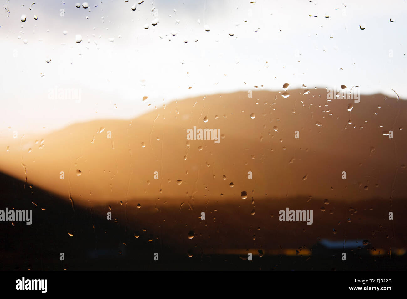 Sunlight breaking through the clouds seen through a raindrop covered window. Stock Photo