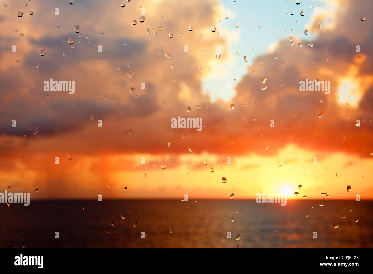 Sunset with tall clouds seen through a raindrop covered window. Stock Photo