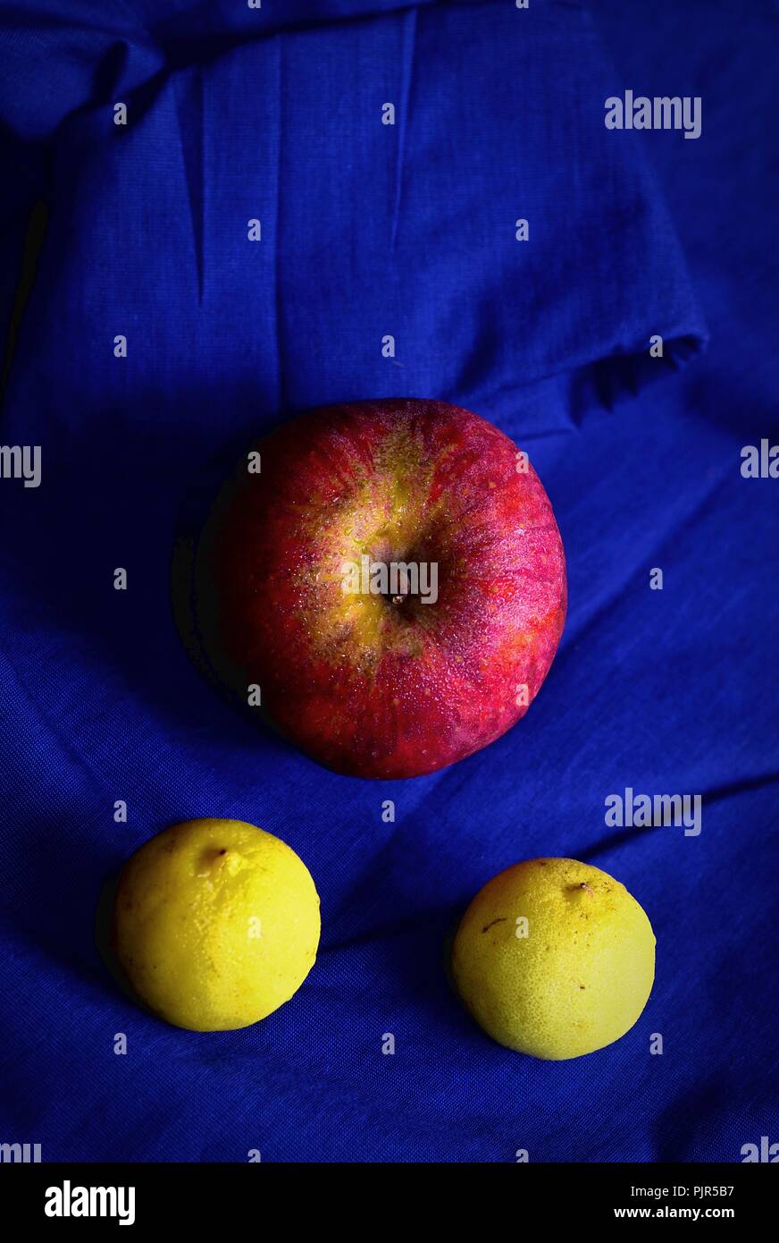 Red sweating apple with two ripe lemons, kept on a blue shirt Stock Photo