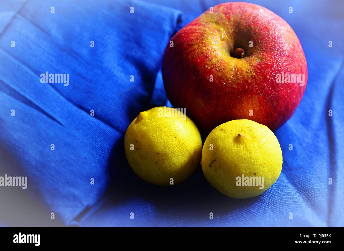 Red sweating apple with two ripe lemons, kept on a blue shirt Stock Photo