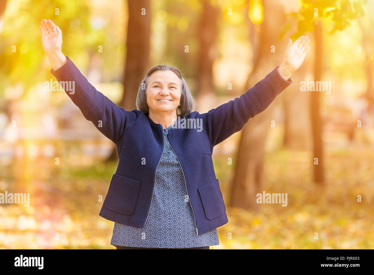 Casual senior woman with arms outstretched standing in autumn park. Stock Photo