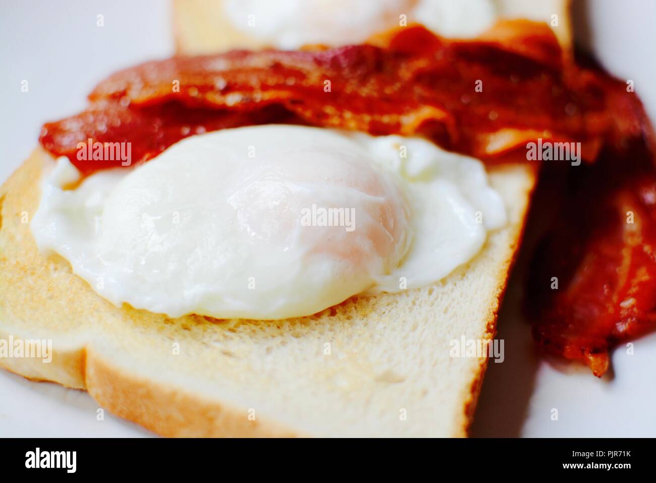 Poached eggs with crispy streaky bacon served on white toast Stock Photo