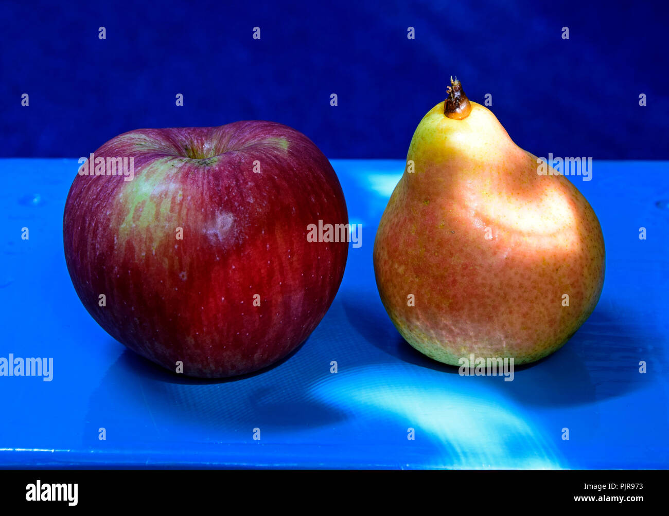A streaked red apple and a yellow pear on a blue table on blue background in close-up lateral view Stock Photo
