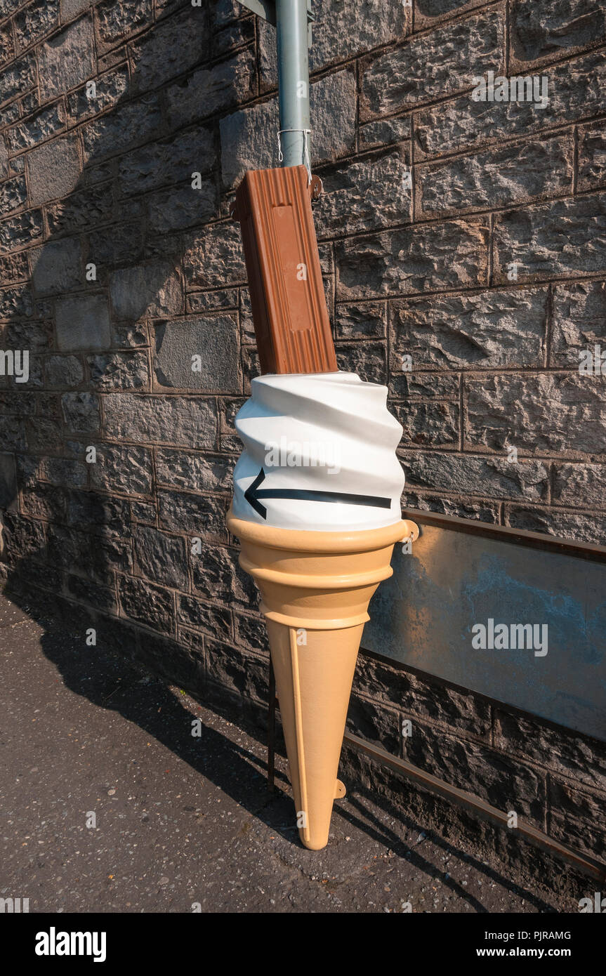 A judiciously placed large plastic ice-cream cornet with a chocolate bar fastened to a signpost against a metal plate on a characteristic stone wall Stock Photo