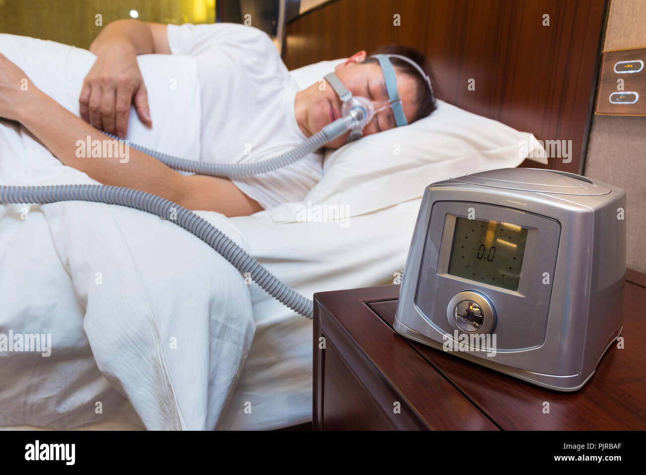 CPAP machine sitting on the bedside table next to the bed with sleeping Asian man wearing