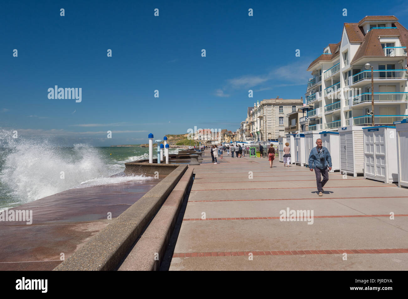 Wimereux, France - 16 June 2018: People walking on the sea front promenade as waves are hitting the sea wall. Stock Photo