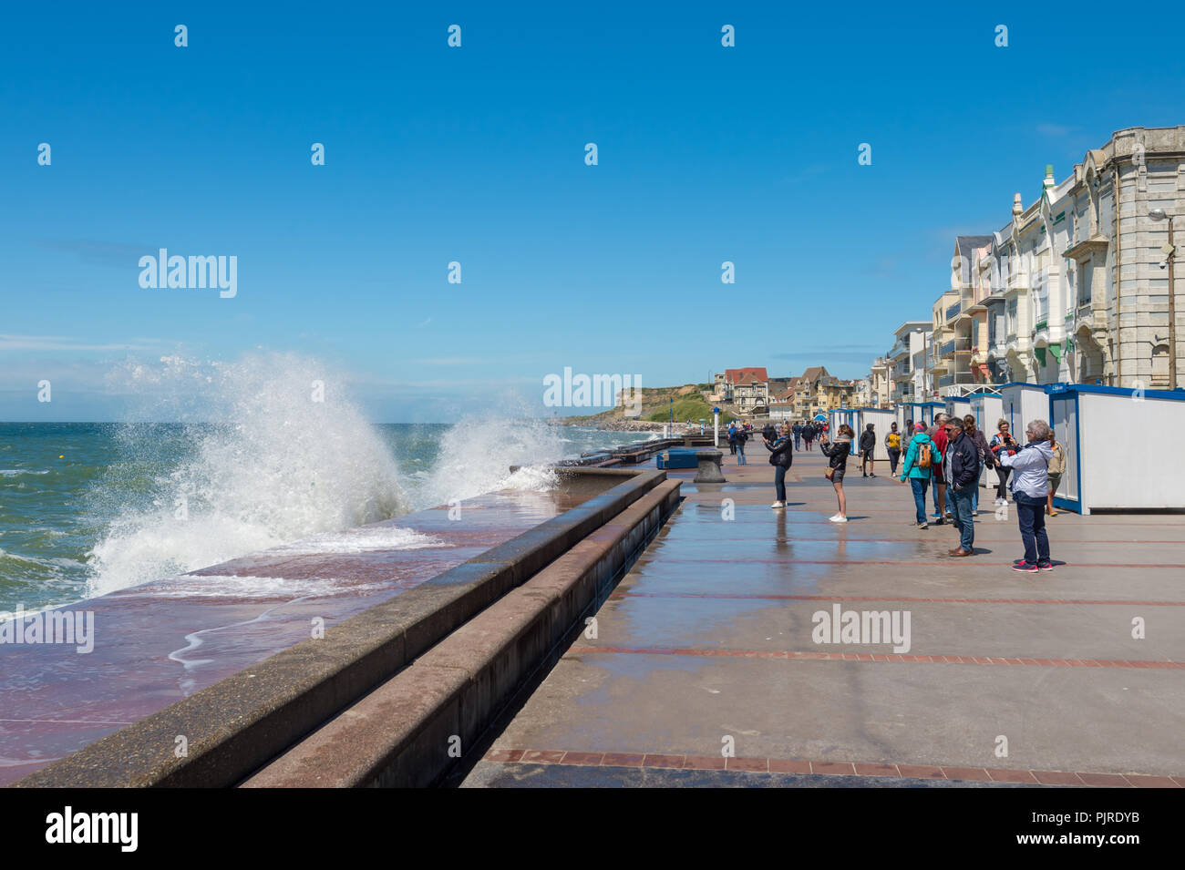 Wimereux, France - 16 June 2018: People walking on the sea front promenade as waves are hitting the sea wall. Stock Photo