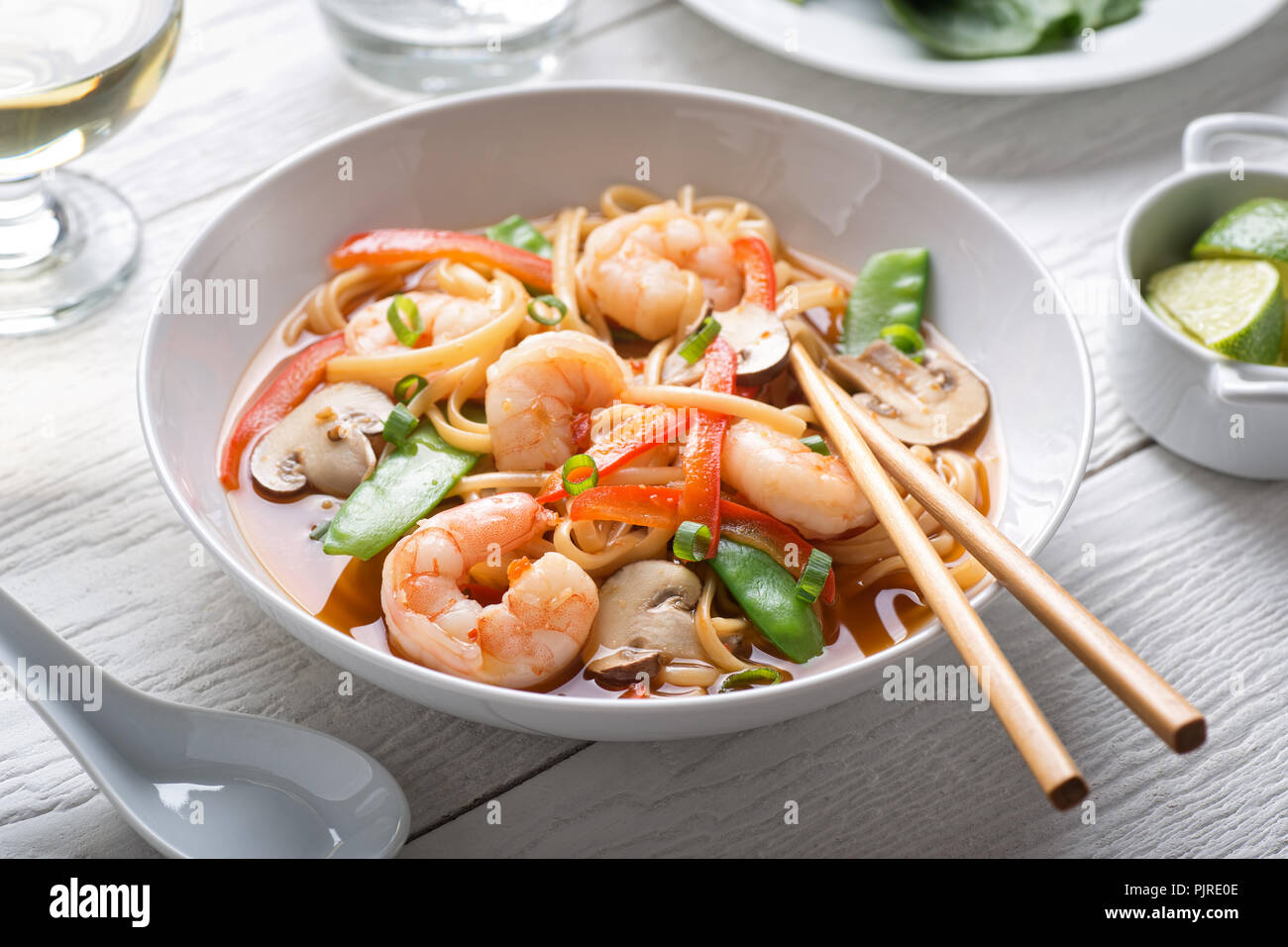 A bowl of delicious spicy asian shrimp noodle soup with mushroom, red pepper, snow peas and scallions. Stock Photo