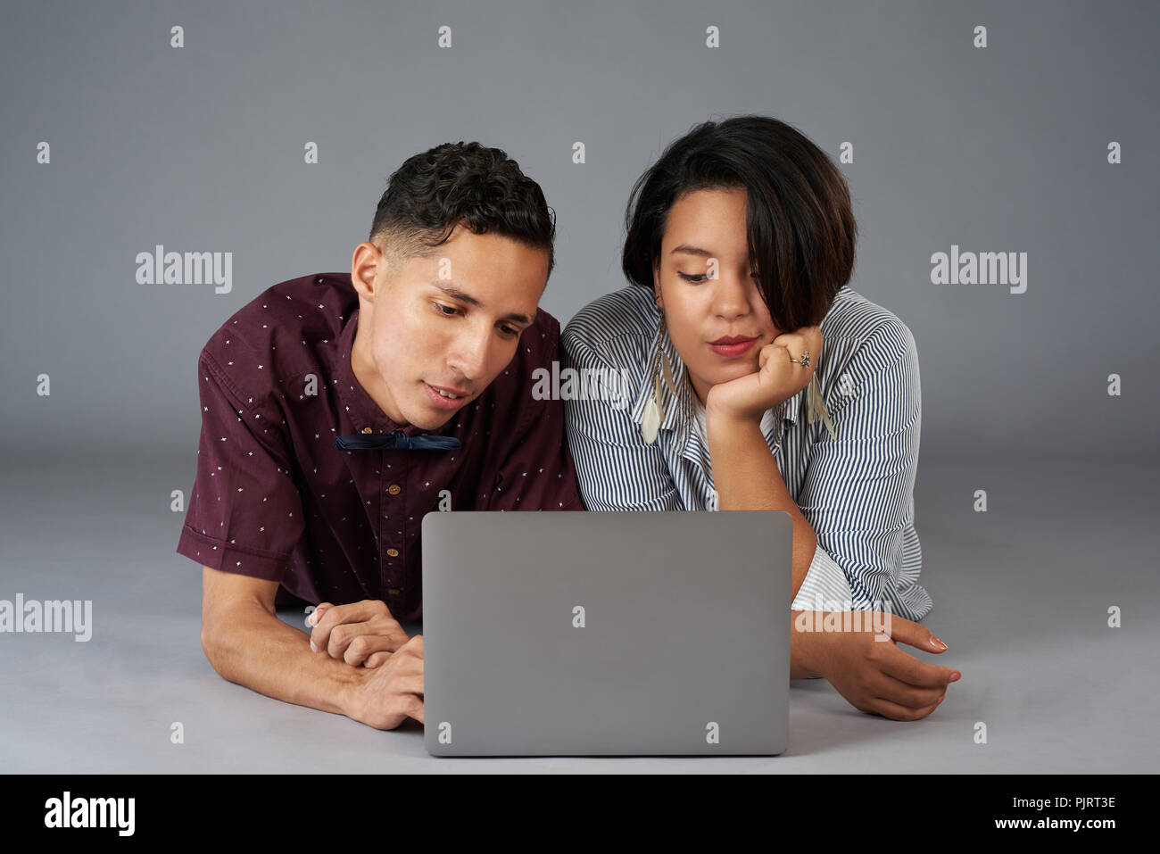 Bored young couple watch movie on laptop isolated on gray studio background Stock Photo