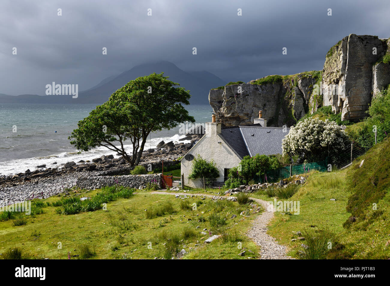 House under cliff at Elgol beach with Red Cuillin Mountains under clouds at Loch Scavaig Scottish Highlands Isle of Skye Scotland UK Stock Photo