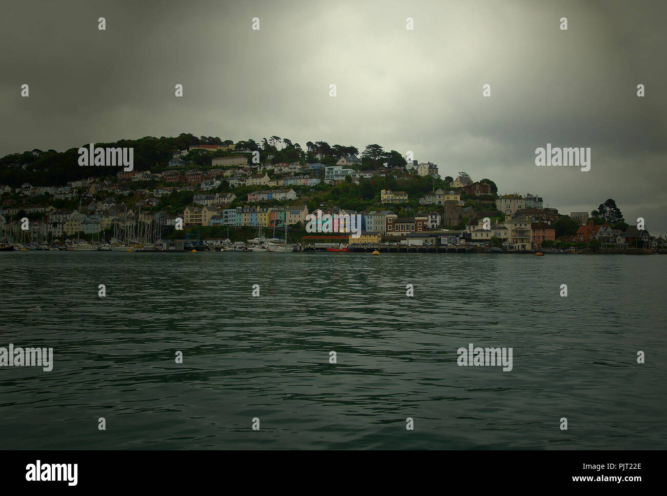 A  view from the river Dart of the town of Kingswear on a summers days with a threatening storm from two directions. Yachts are moored close into the Stock Photo