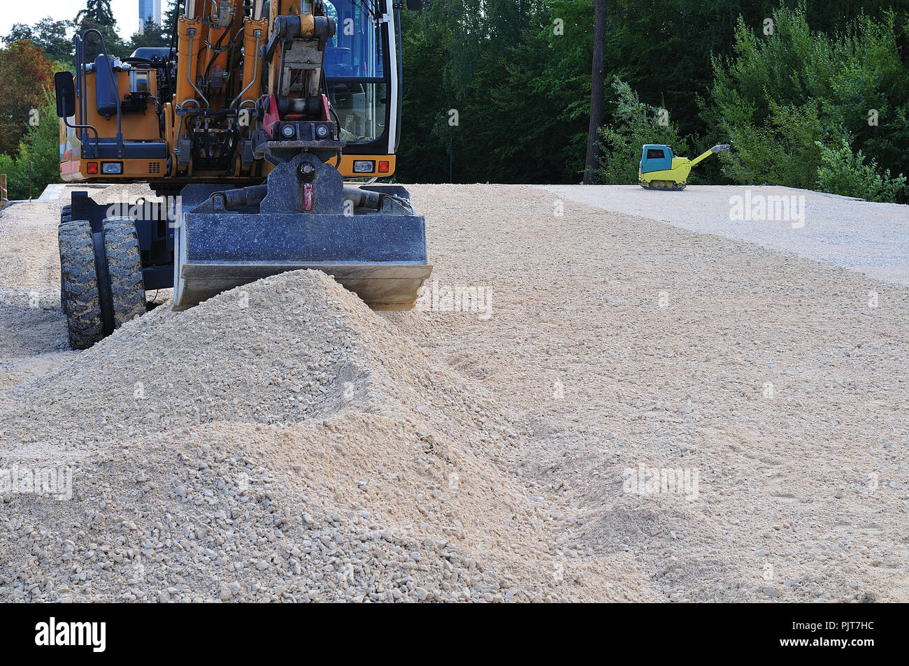 digger and vibrating machine at construction site with limestone gravel to be nivellated Stock Photo