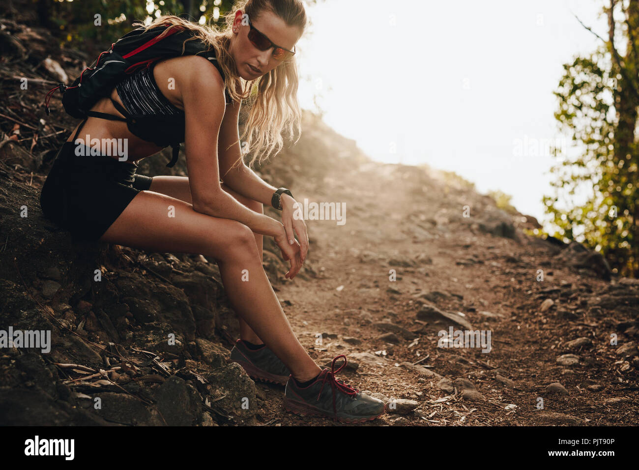 Athletic girl resting on rocks after a hard training in the mountains. Woman trail runner taking a break after running exercise. Stock Photo