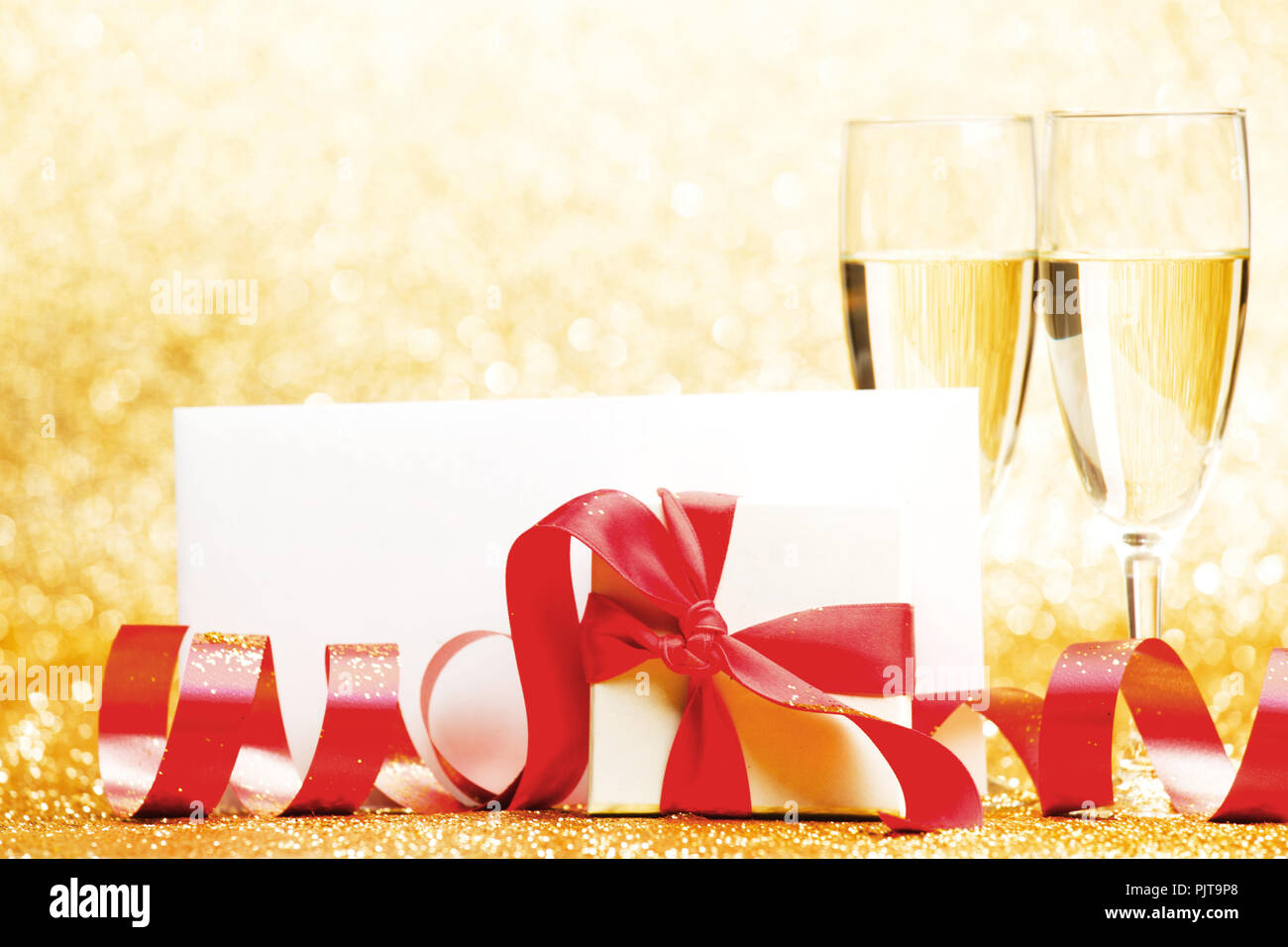 Champagne glasses and present in whitebox with red ribbon on golden background Stock Photo