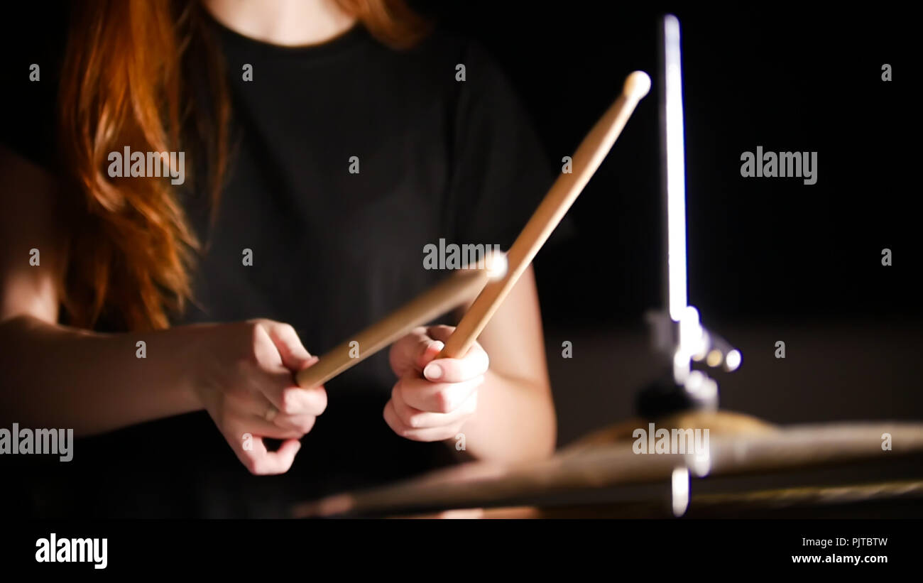 Redhaired girl plays music drums in a dark studio. Hands, drum sticks