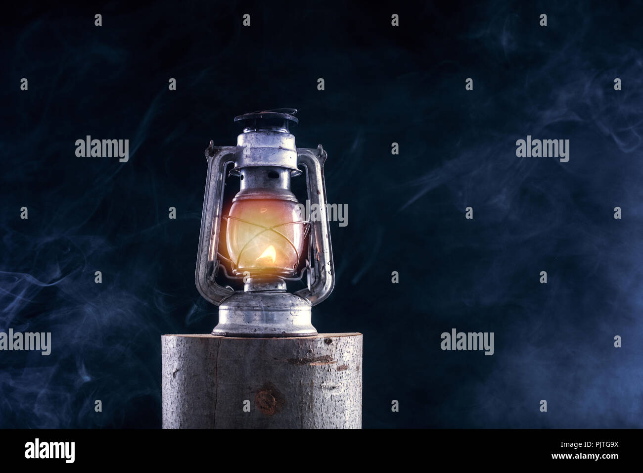 Old oil lamp burning at lumber log and foggy smoke dark night