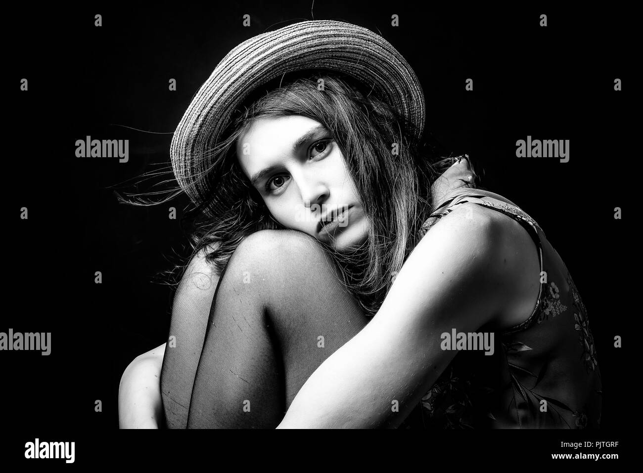 Studio image of a young woman sitting on a stool hugging her knees in a ...
