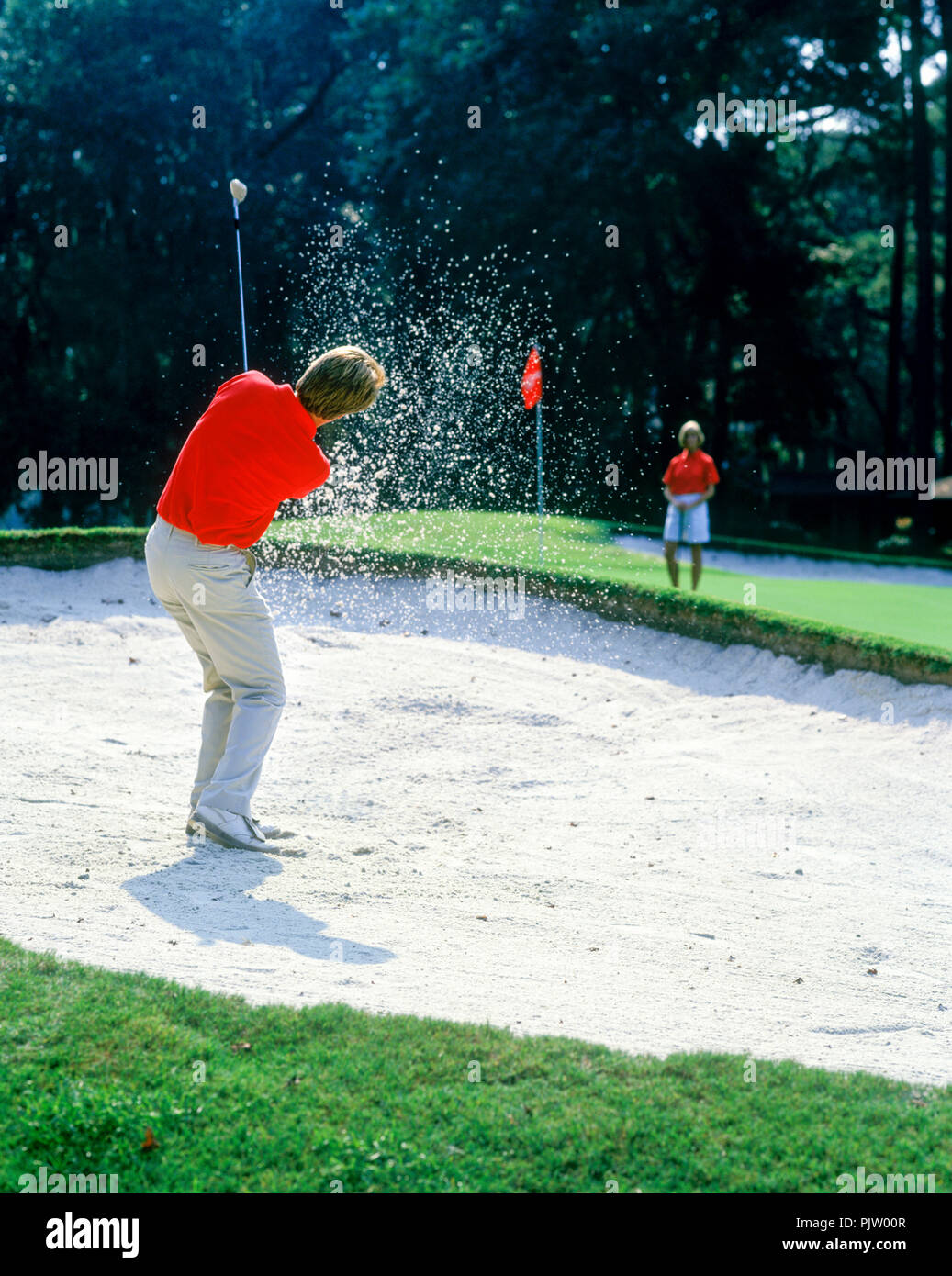 1990 HISTORICAL MALE GOLFER HITS BALL OUT OF SAND TRAP ON TO PUTTING GREEN Stock Photo
