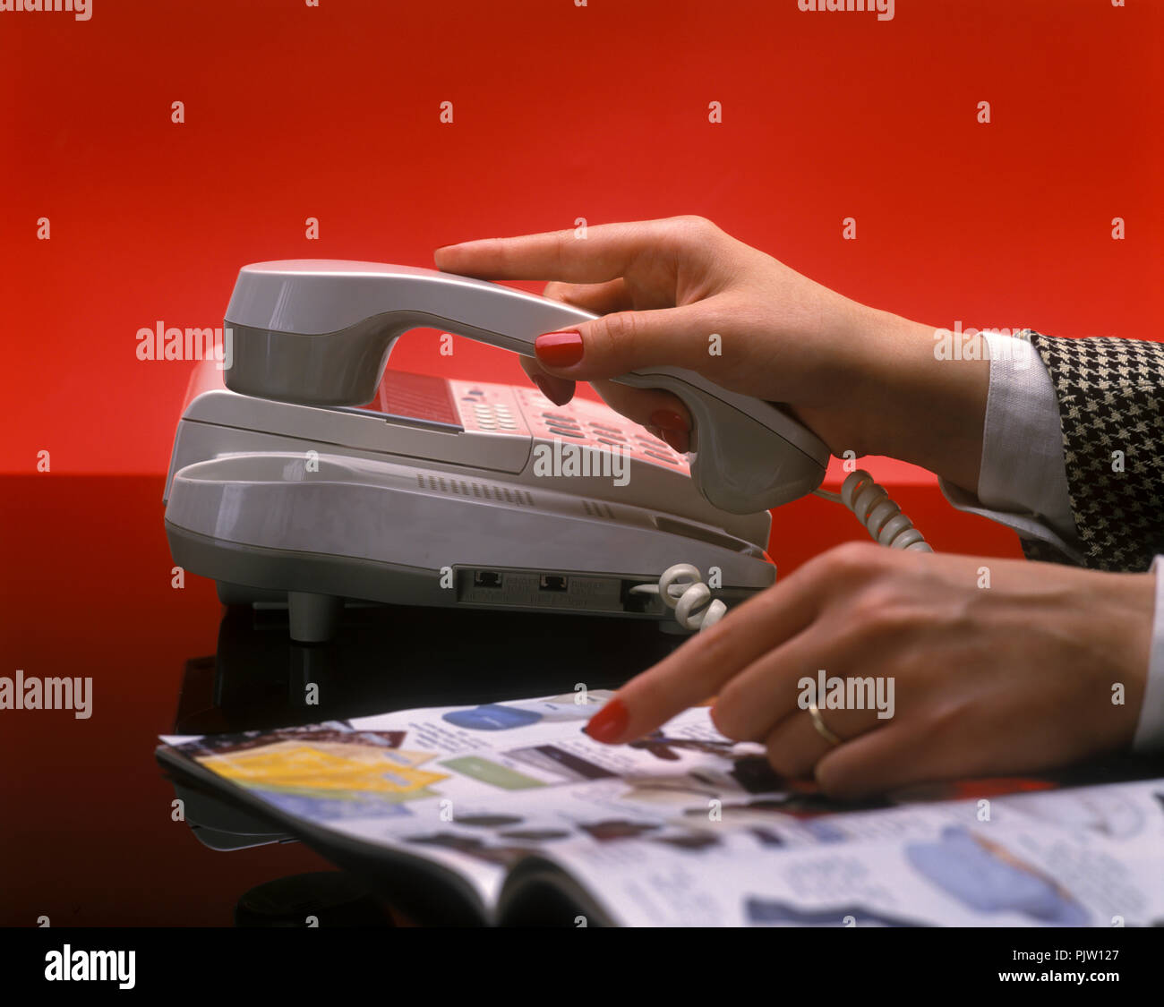 1991 HISTORICAL WOMAN’S HANDS PAPER CATALOG SHOPPING ON PLAIN RED BACKGROUND Stock Photo