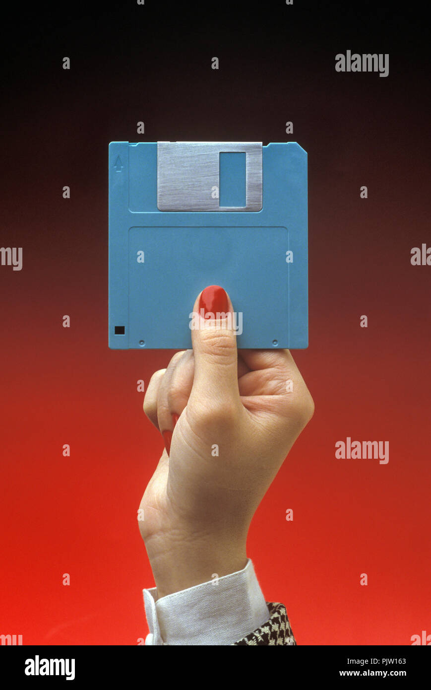 1991 HISTORICAL WOMAN’S HAND AND 3.5 INCH FLOPPY COMPUTER DISCS ON PLAIN RED BACKGROUND (©IBM 1973) Stock Photo