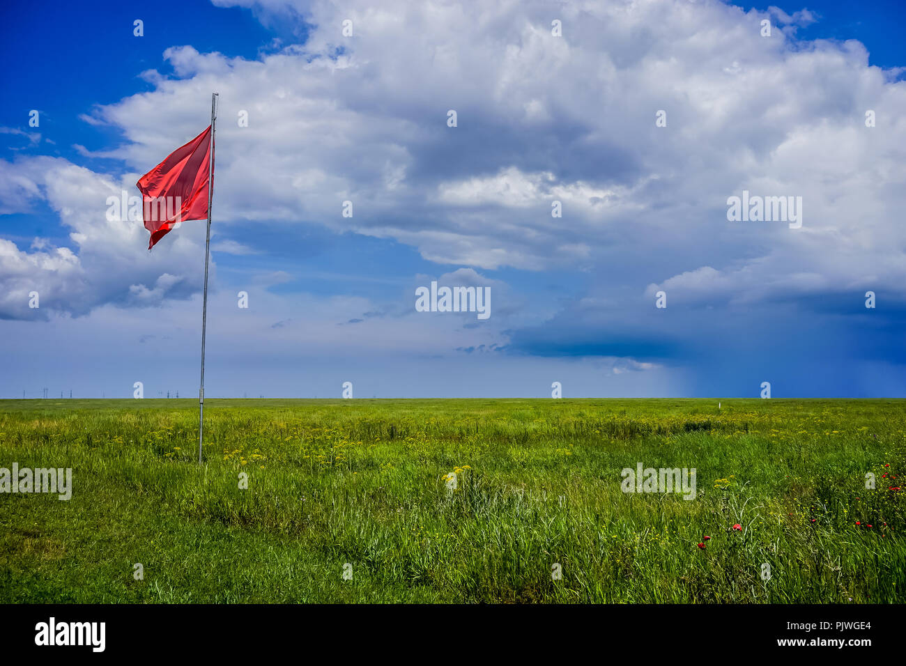 Waving the scarlet flag over the green steppe on the background of blue sky and clouds Stock Photo