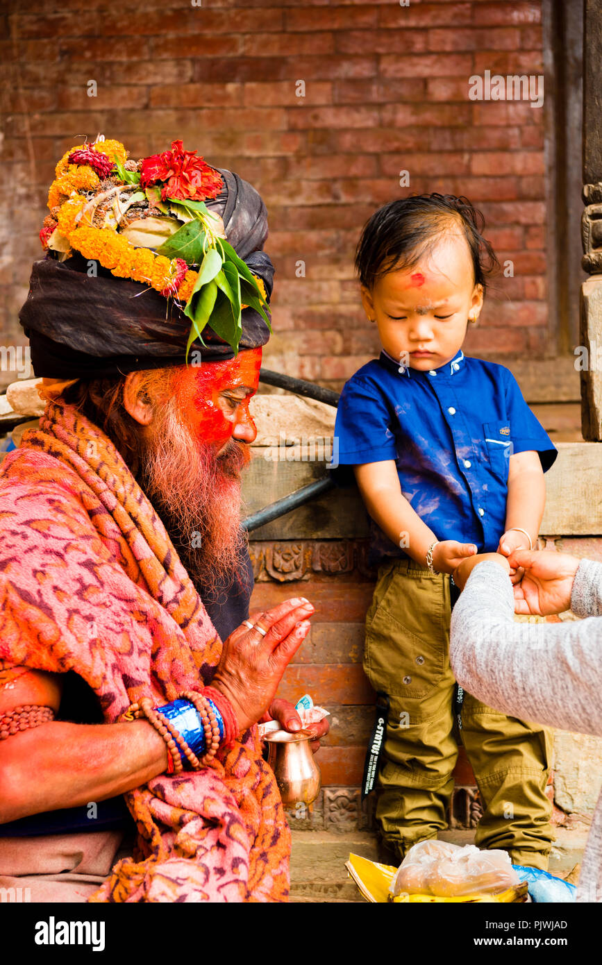 Pashupatinath, Nepal - July 17, 2018 : Holy Sadhu man with traditional painted face and colouful clothes is blessing a child at Pashupatinath Stock Photo