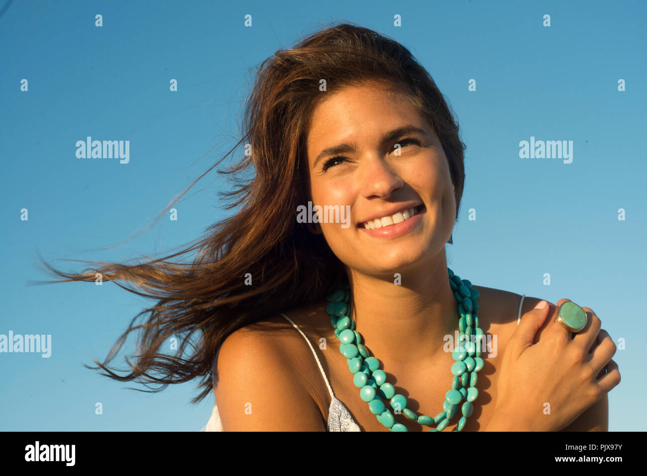 Young woman wearing with long brown flyaway hair against blue sky Stock Photo