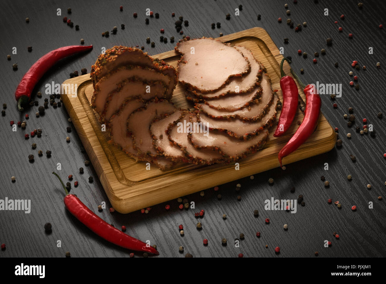 slices of ham on wooden board with red pepper closeup Stock Photo