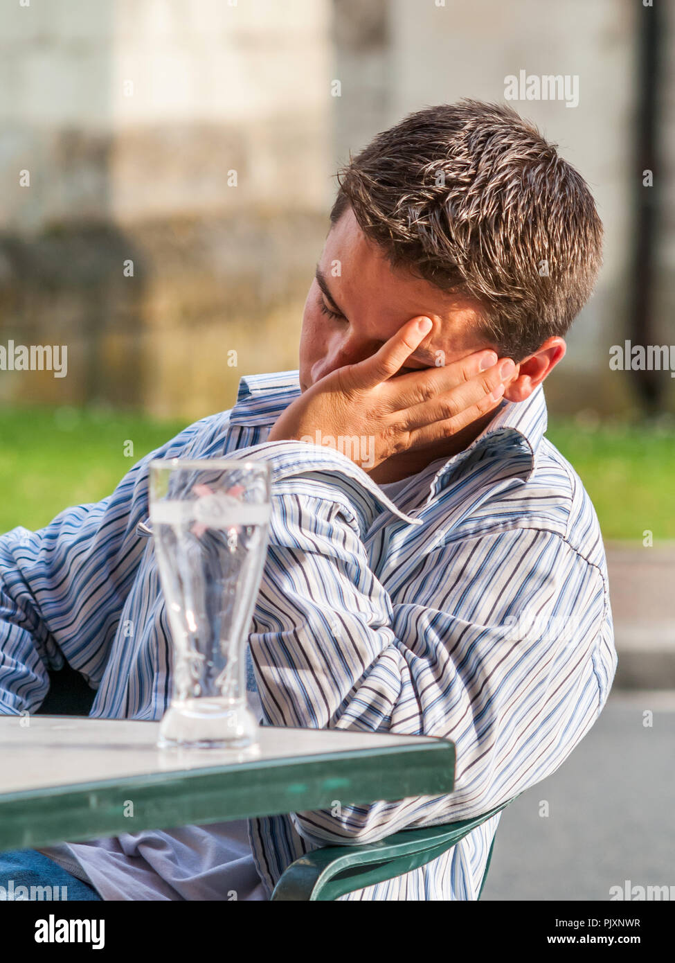 Young man asleep at outside bar table after drinking - France. Stock Photo