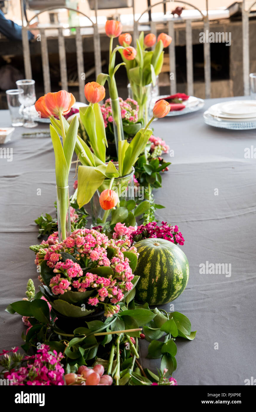 A floral arrangement of lovely orange flowers with colourful pink bunch in foreground with an enticing round watermelon & grapes. Stock Photo