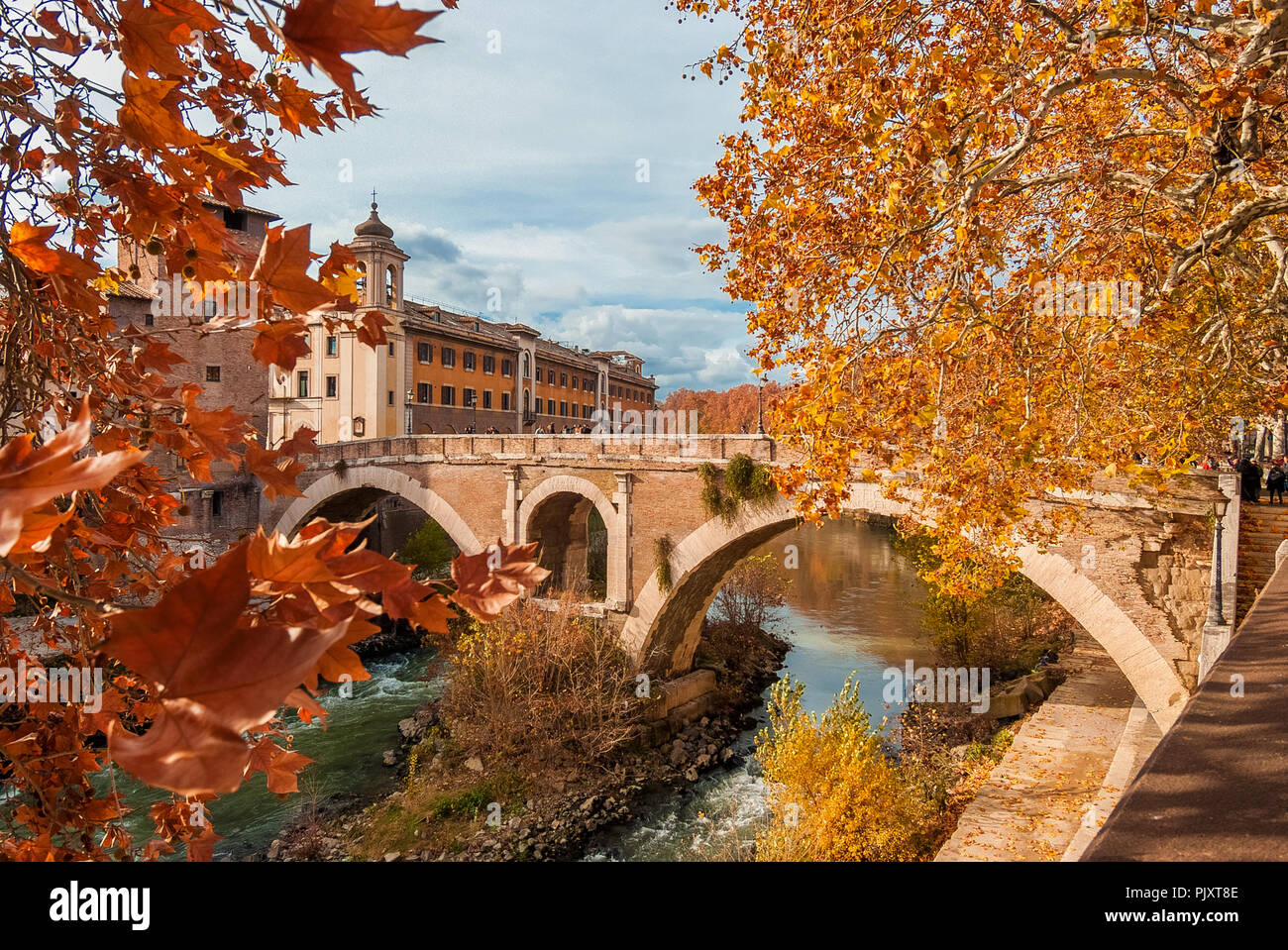 Autumn and foliage in Rome. Red and yellow leaves near Tiber Island with ancient roman bridge, in the city historic center Stock Photo