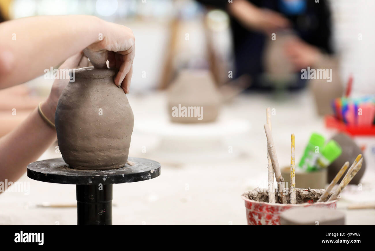 students working with clay getting their hands dirty. Visual art class showing hands on a coil pot with clay tools and desk in background. Art educati Stock Photo