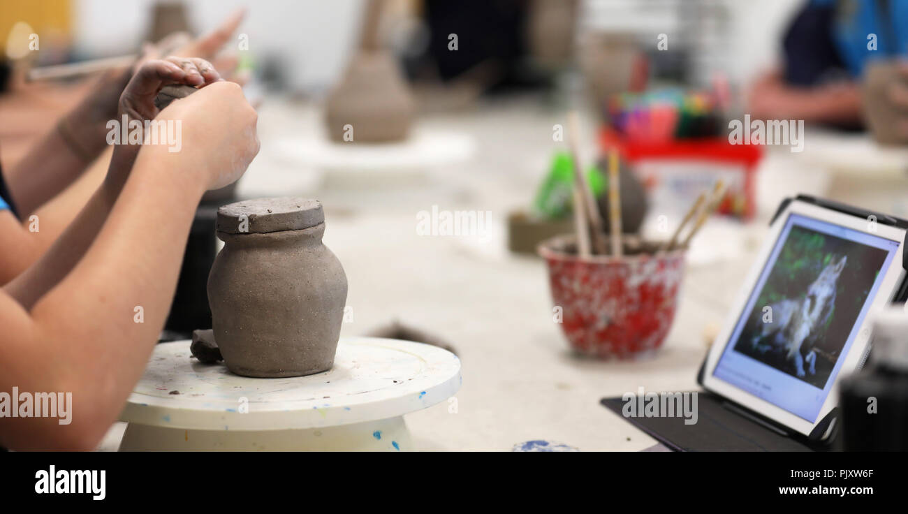 High school students working with clay in the classroom and a digital device tablet for research. ceramic visual art class. education and technology Stock Photo