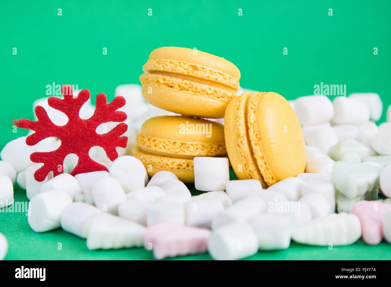 Yellow macaroons, marshmallow and red flake on green Stock Photo