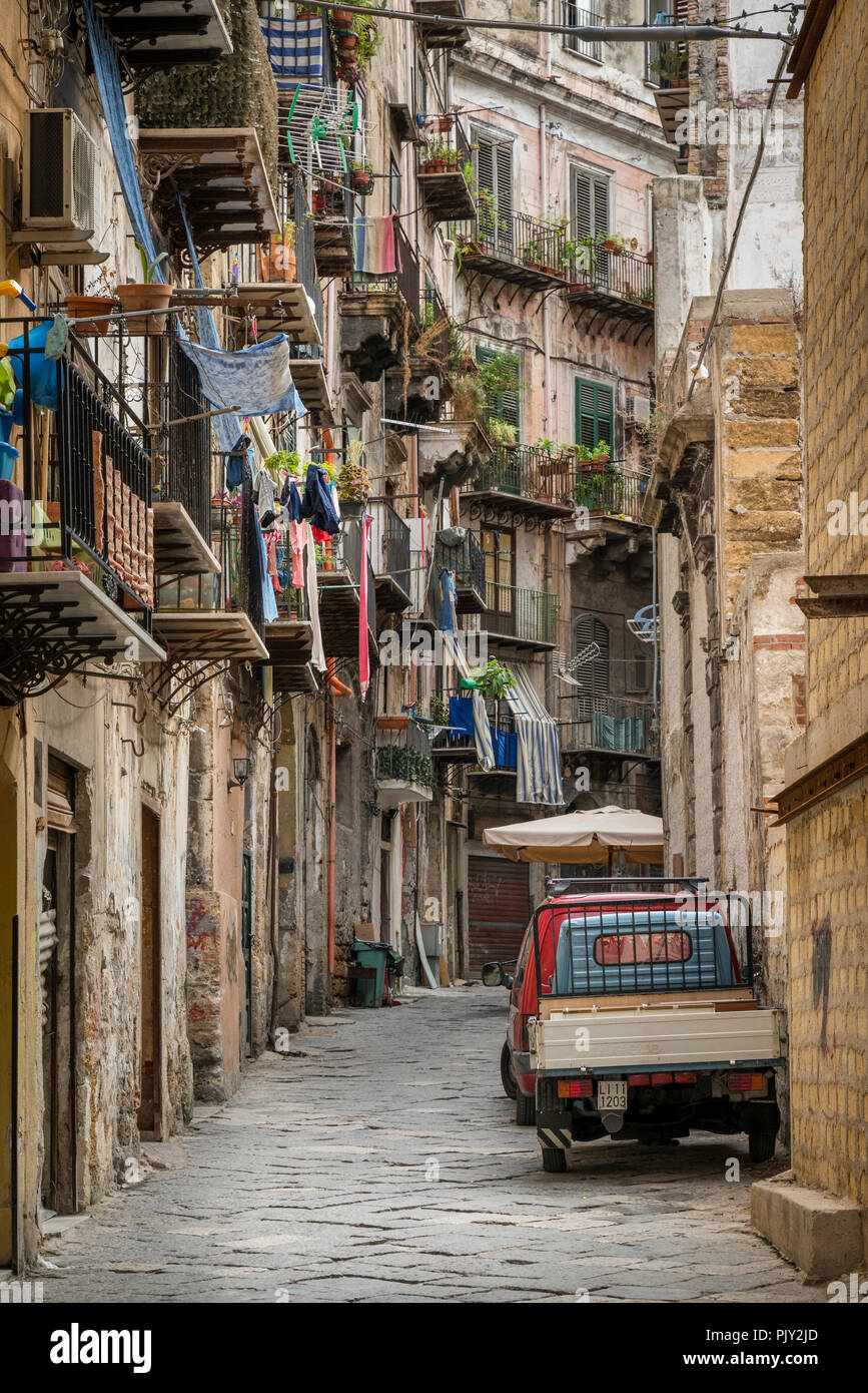 A Palermo street scene with washing hanging from the balconies of residential apartments and a traditional Piaggio Ape three wheeled van parked outsid Stock Photo