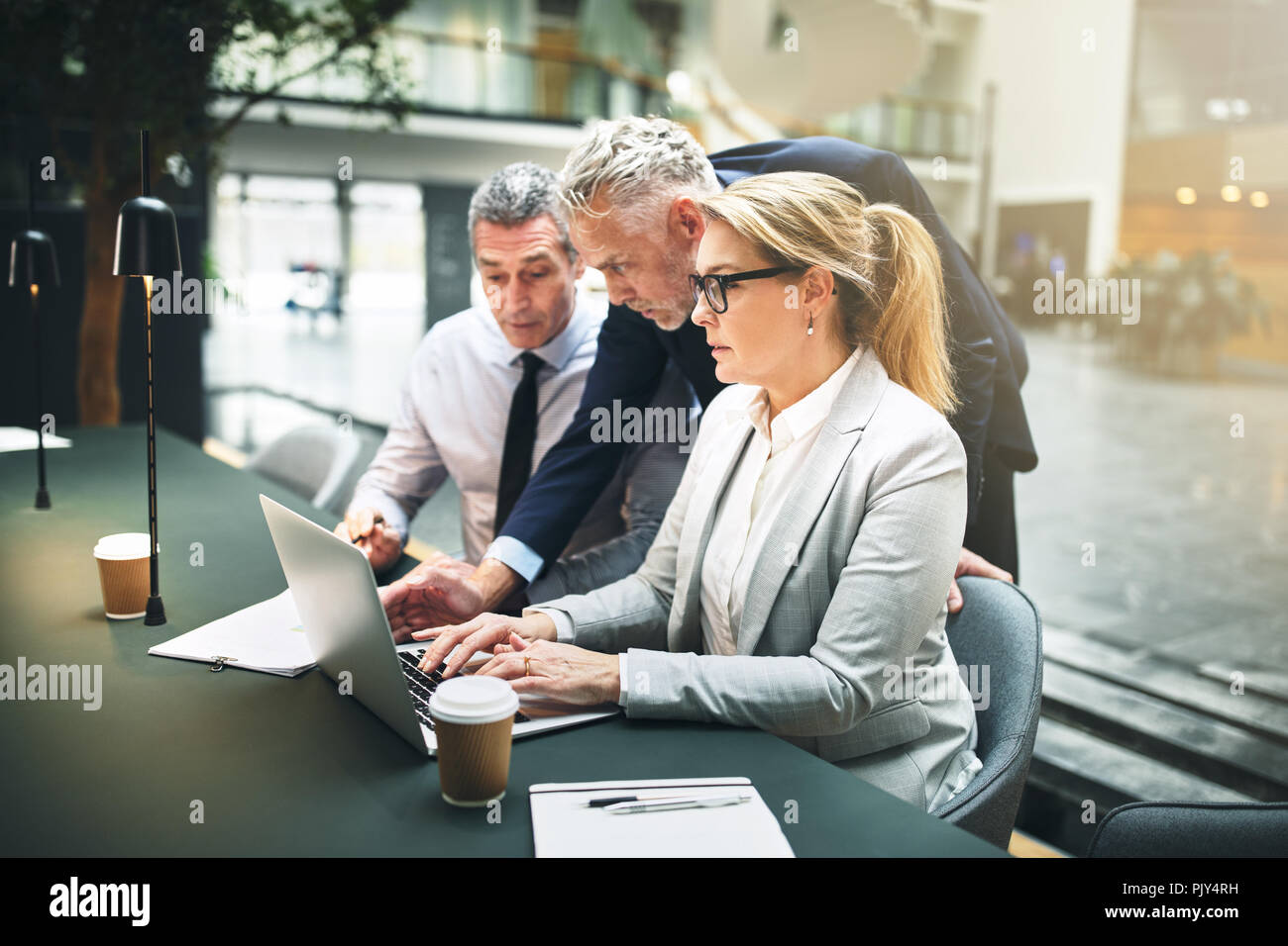 Mature manager and two businesspeople working together on a laptop during a meeting in the lobby of a modern office Stock Photo