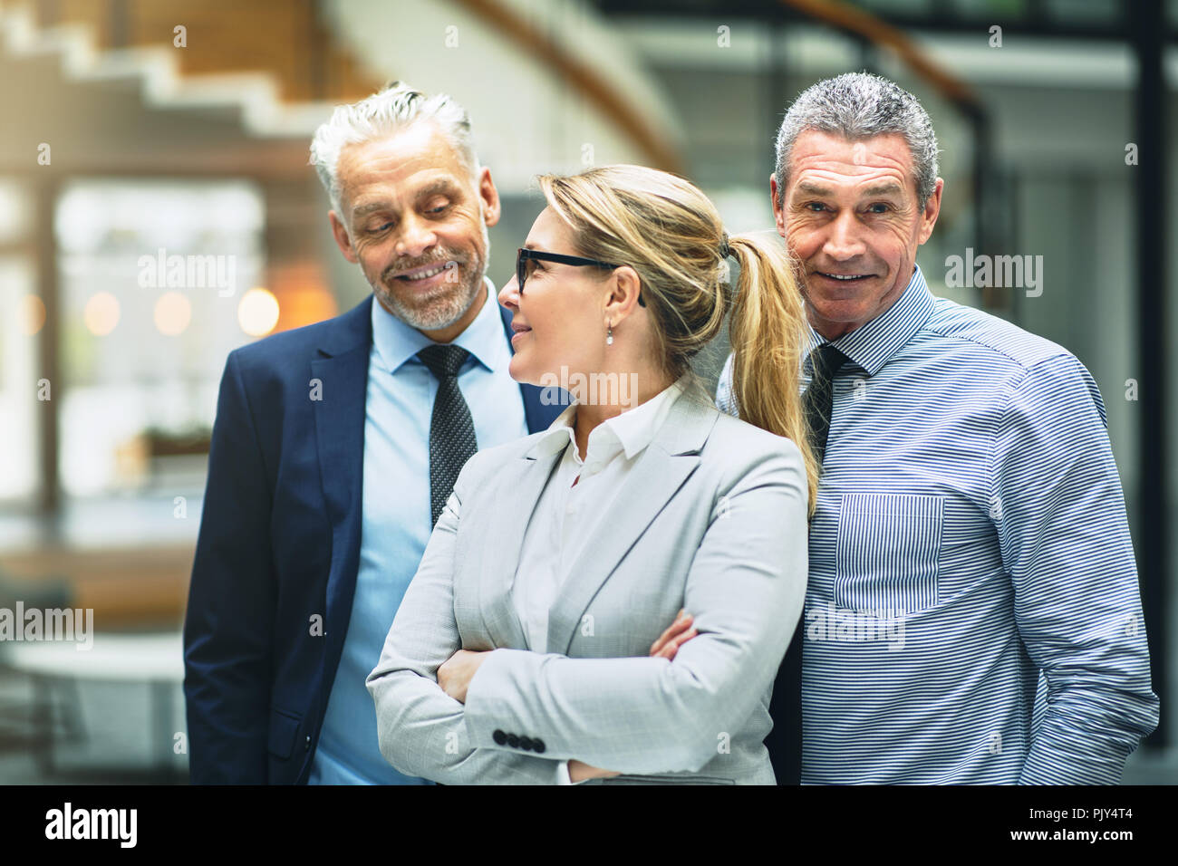 Smiling mature businesswoman talking with two male colleagues while standing together in the lobby of a modern office building Stock Photo