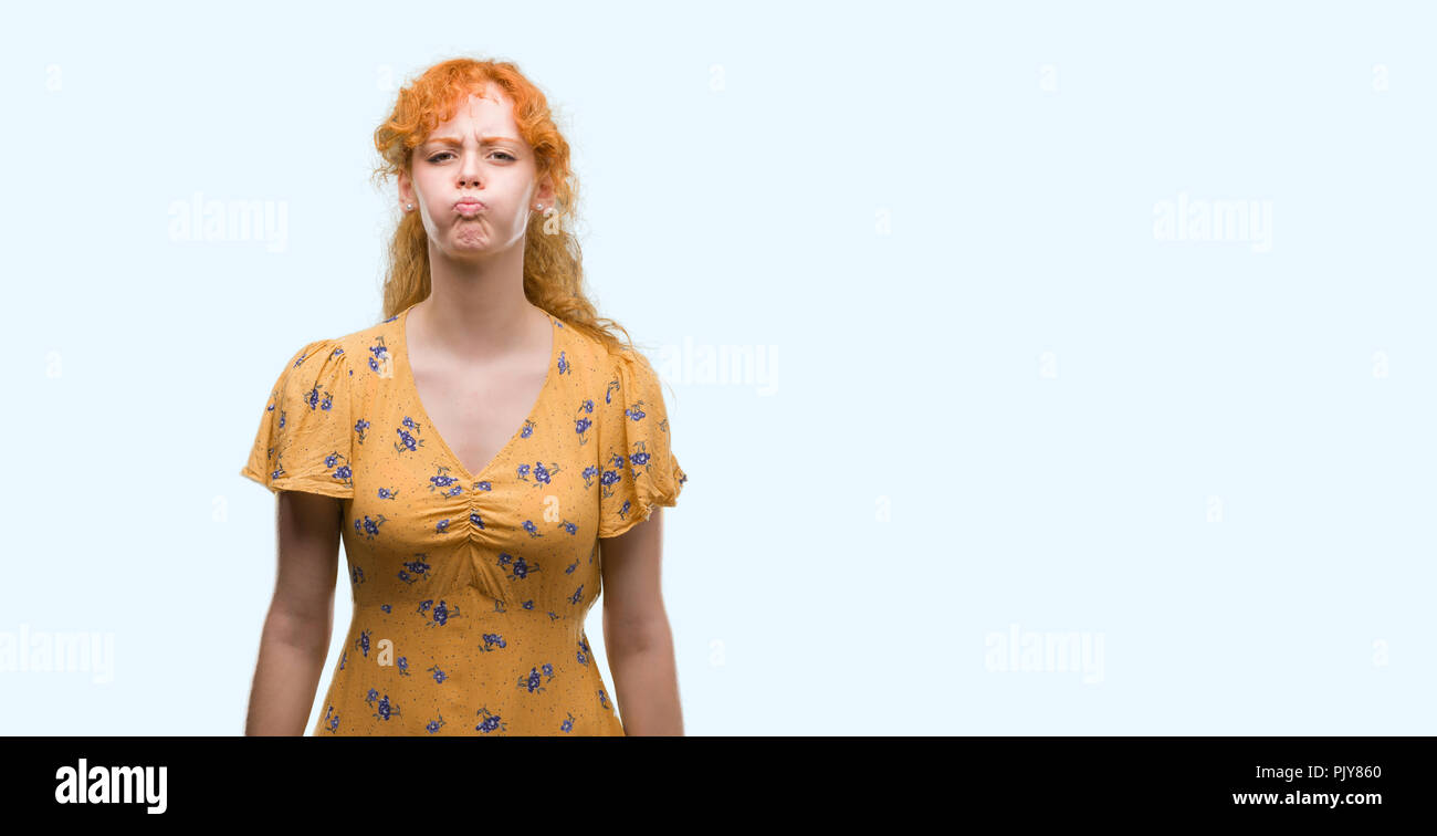 Young redhead woman puffing cheeks with funny face. Mouth inflated with