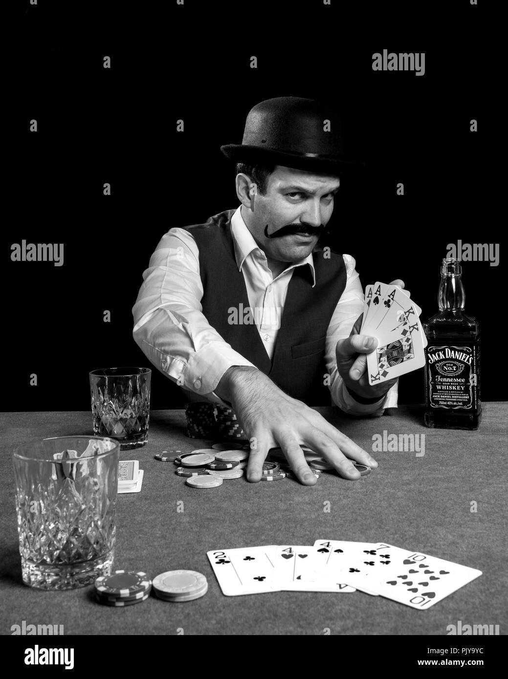 Photography of a man playing and winning a game of poker drinking a bottle of jack daniel's whisky fake vintage old melon hat, alcohol Stock Photo