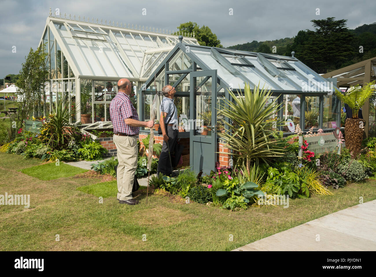 2 men look closely at framework of greenhouse for sale on attractive outdoor trade stand display - RHS Chatsworth Flower Show, Derbyshire, England, UK Stock Photo