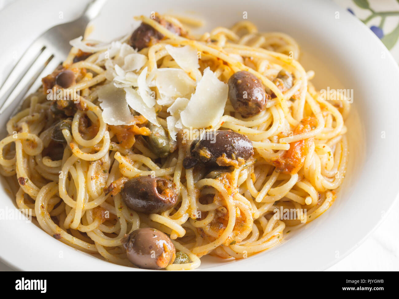Spaghetti with anchovies, capers and black olives close up topped with parmigiano cheese shavings Stock Photo