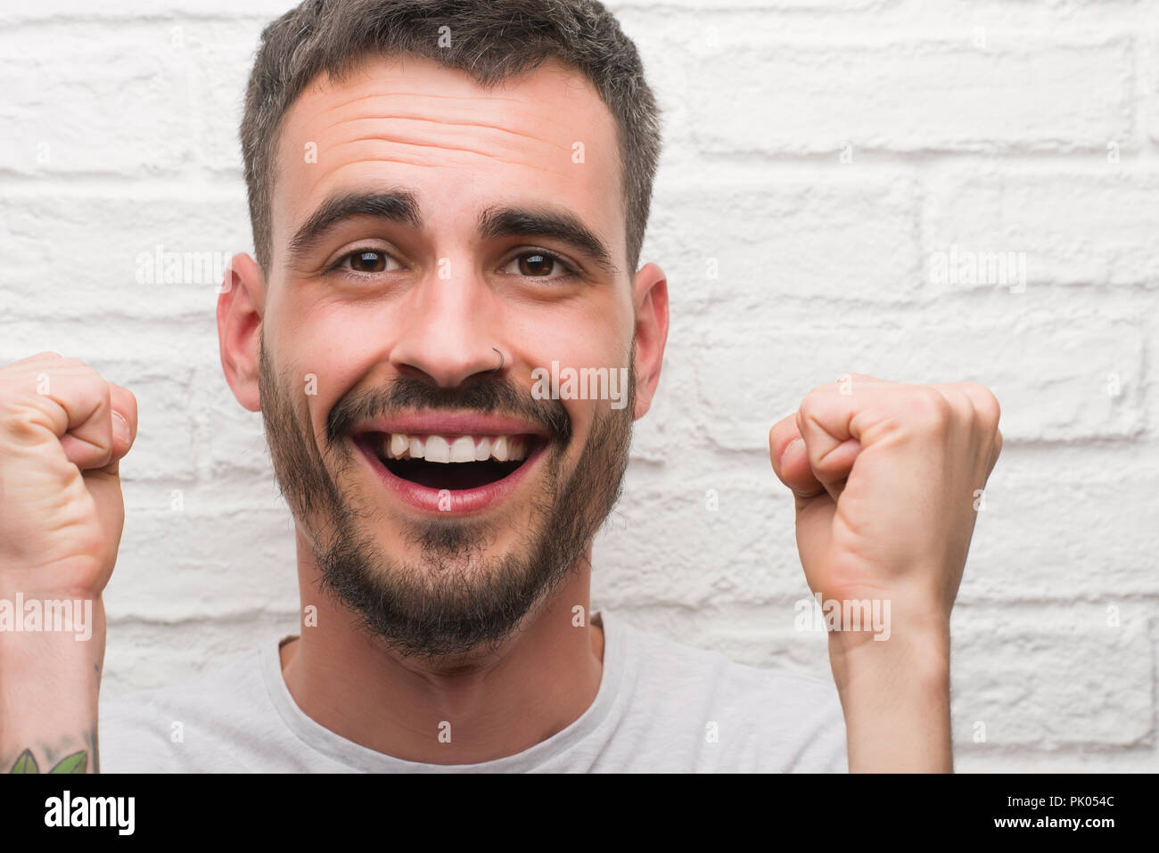 Young adult man standing over white brick wall screaming proud and