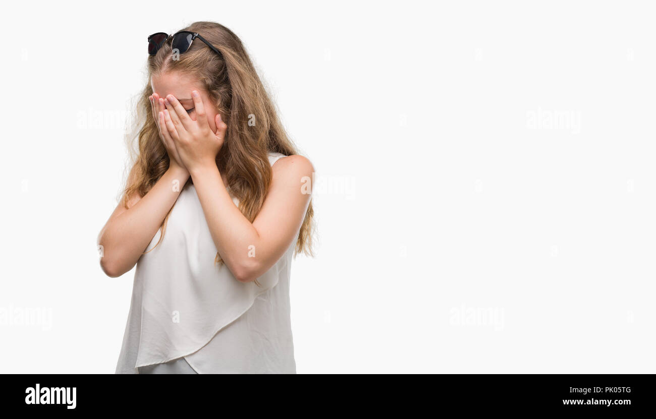 Young blonde woman wearing sunglasses with sad expression covering face with hands while crying. Depression concept. Stock Photo