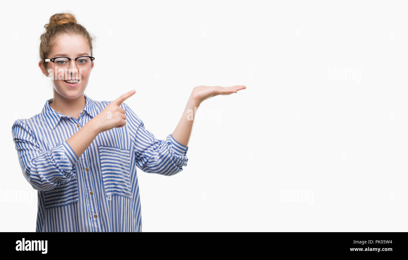 Young blonde business woman amazed and smiling to the camera while presenting with hand and pointing with finger. Stock Photo