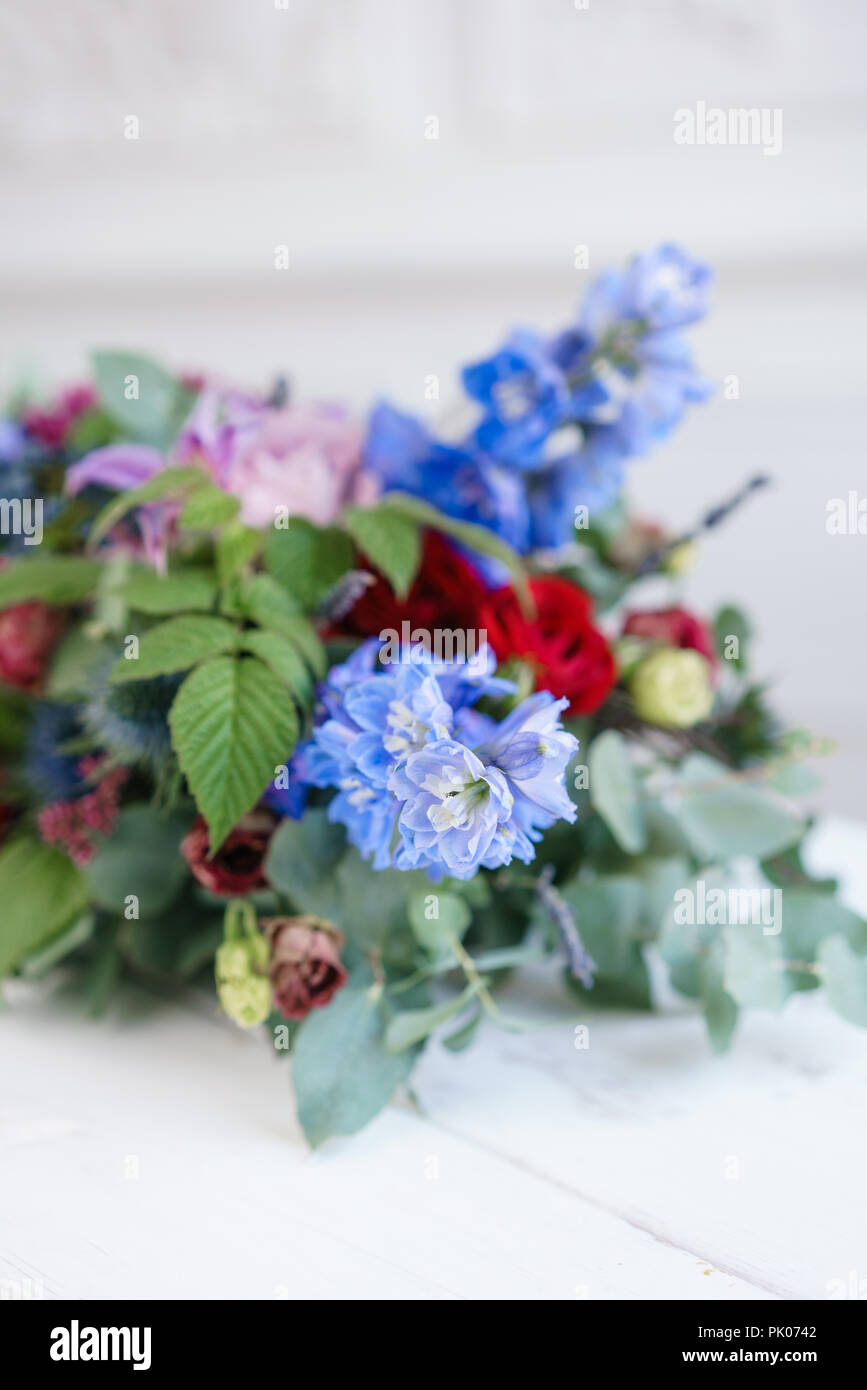 selective focus. Elongated floral arrangement in vintage metal vase. table setting. Blue and red color. Gorgeous bouquet of different flowers. Bright room, stucco on the wall Stock Photo