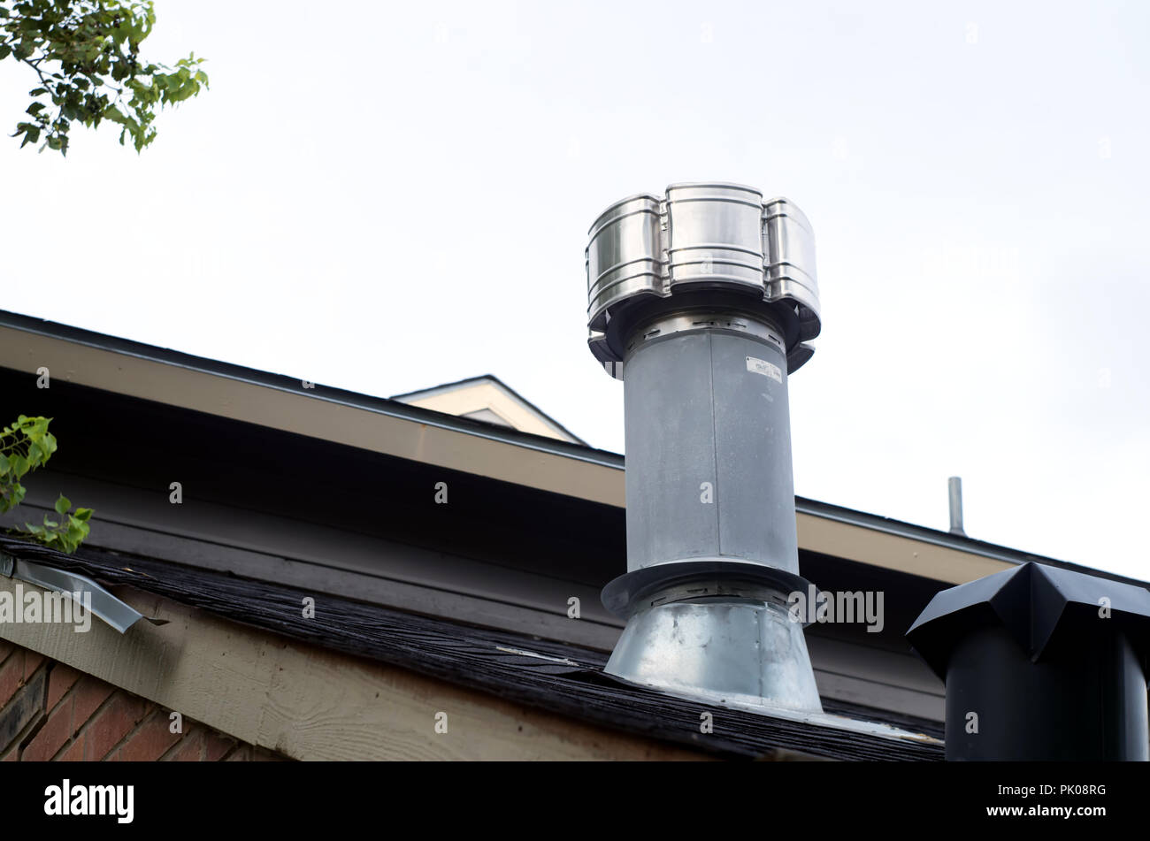 Exhaust stack from a gas fired water boiler mounted on shingled roof. Stock Photo