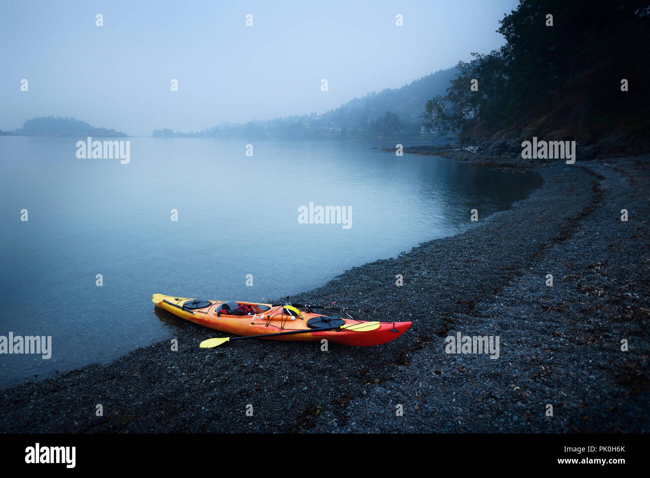 Red kayak on the Salish sea shore in yearly morning mist. Nanaimo, Vancouver Island, British Columbia, Canada. Stock Photo