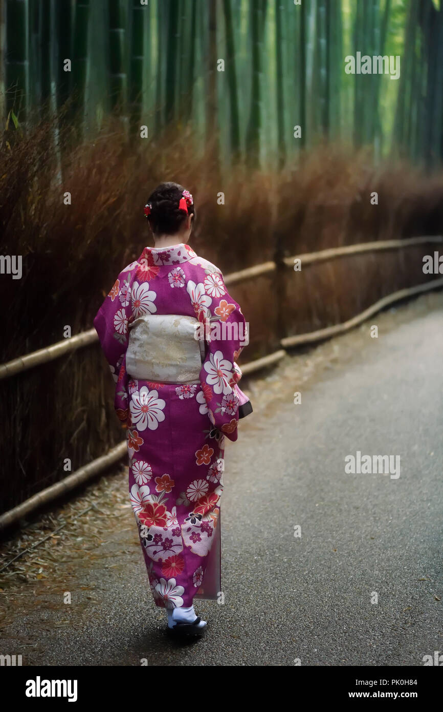 Young Japanese woman in a purple kimino walking along Arashiyama bamboo forest in Kyoto, Japan. Stock Photo