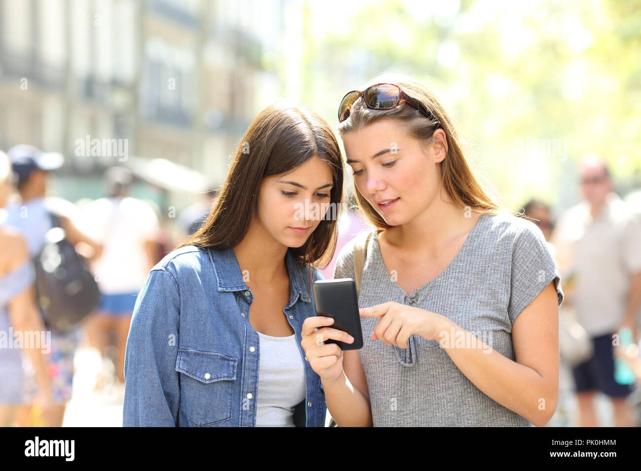 Two girls talking about online content in a smart phone in the street Stock Photo