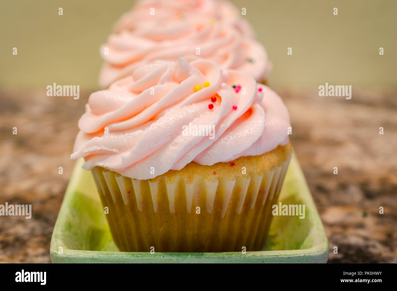 Light pink butter cream frosting swirled on top of fresh homemade cupcake. Colorful candy sprinkles sprinkled on top. Delicious sweet treat for party. Stock Photo
